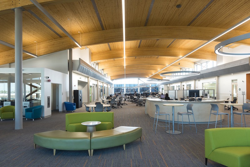 Interior view of the library space at Algonquin College. Low sofas and bar tables and stools are seen in the foreground, with a reference desk.