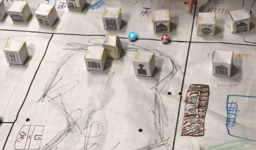 Cardboard buildings on top of a paper map with roads and movement recorded in pencil and crayons.