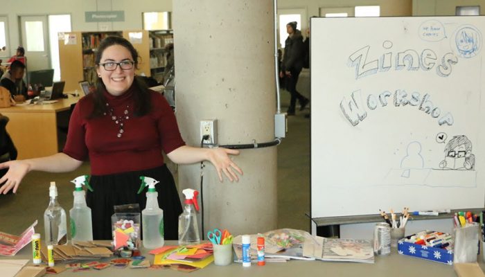 Woman Standing At Table With Craft Supplies For Zine Workshop