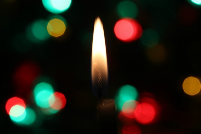 Candle burning in dark background with red, white and green lights