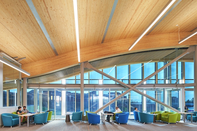 Interior view of the new library at Algonquin College. A row of tables and colourful chairs can be seen in front of a glass wall, some chairs are occupied by patrons.