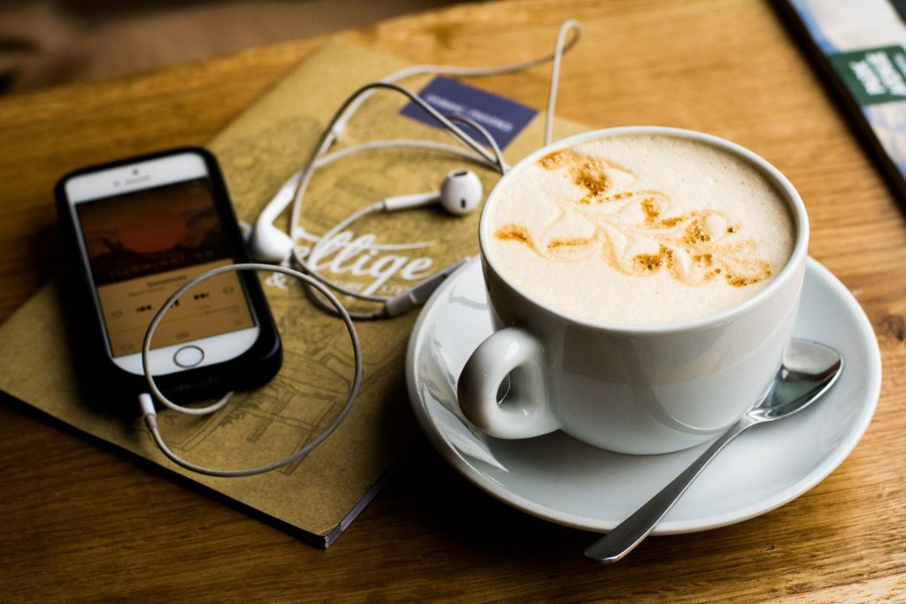 Photo of a full coffee cup and cell phone with headphones attached.