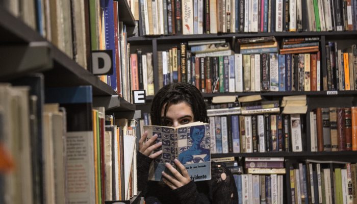 Photo Of A Woman Surrounded By Books, Covering Her Face With A Copy Of 1984.