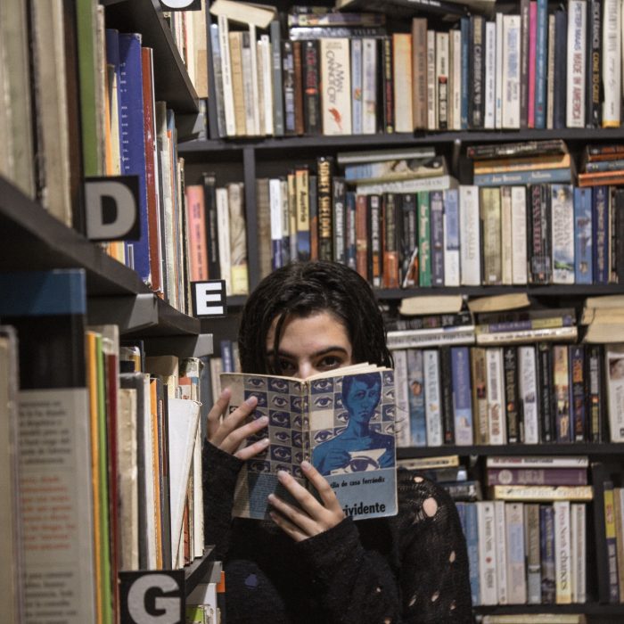 Photo Of A Woman Surrounded By Books, Covering Her Face With A Copy Of 1984.
