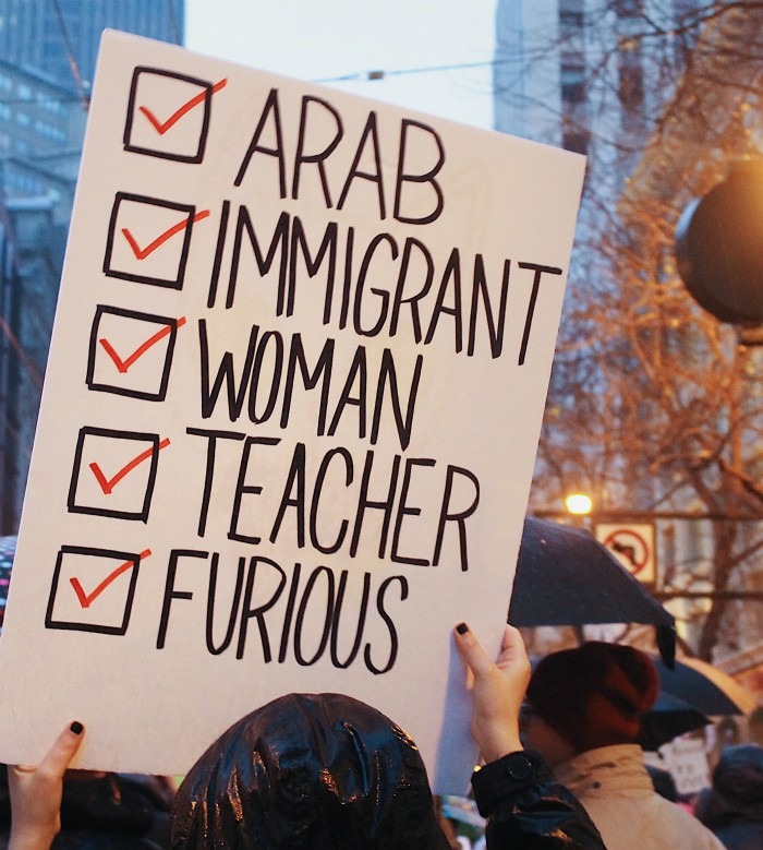 A woman is holding a poster with words arab, woman, immigrant, teacher, furious checked off.