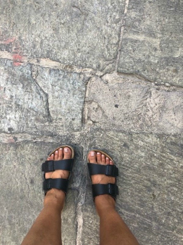 A pair of feet in sandals on a concrete sidewalk