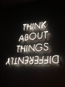 A neon sign with the words "think about things differently", with the last word reversed.