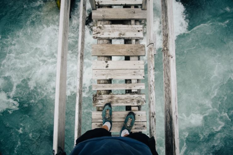 A person is standing on a wooden bridge looking down at rushing water.