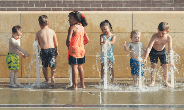 Six children of various ages standing in front of jets of water