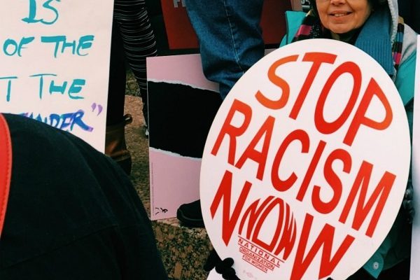 A Woman Sitting Holding A Sign That Says Stop Racism Now