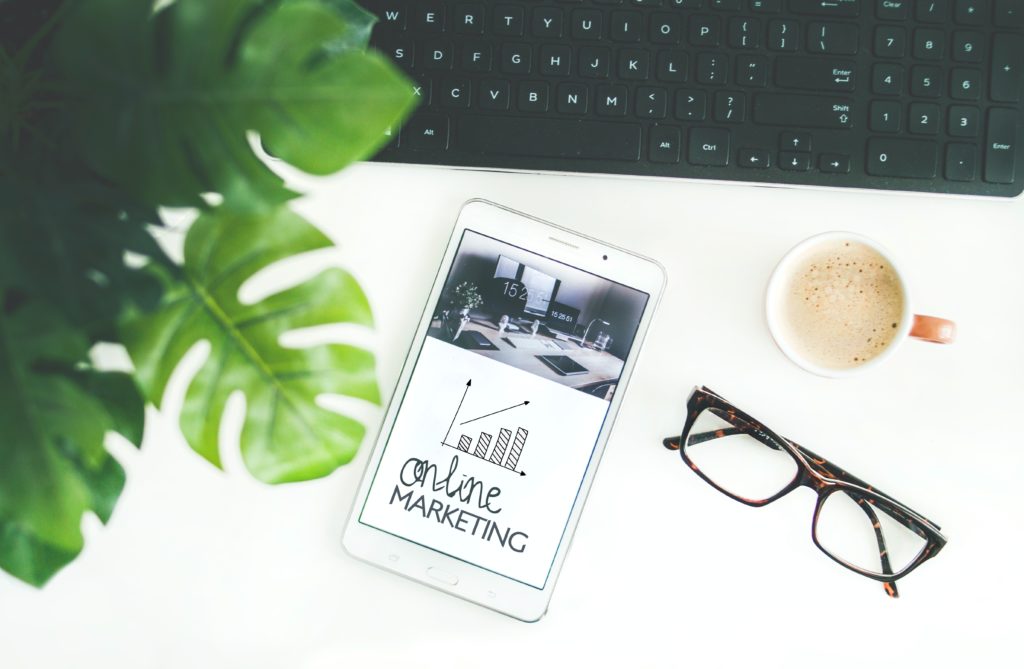 Coffee mug, eyeglasses, plant and laptop surrounding a cellphone that reads "online marketing".