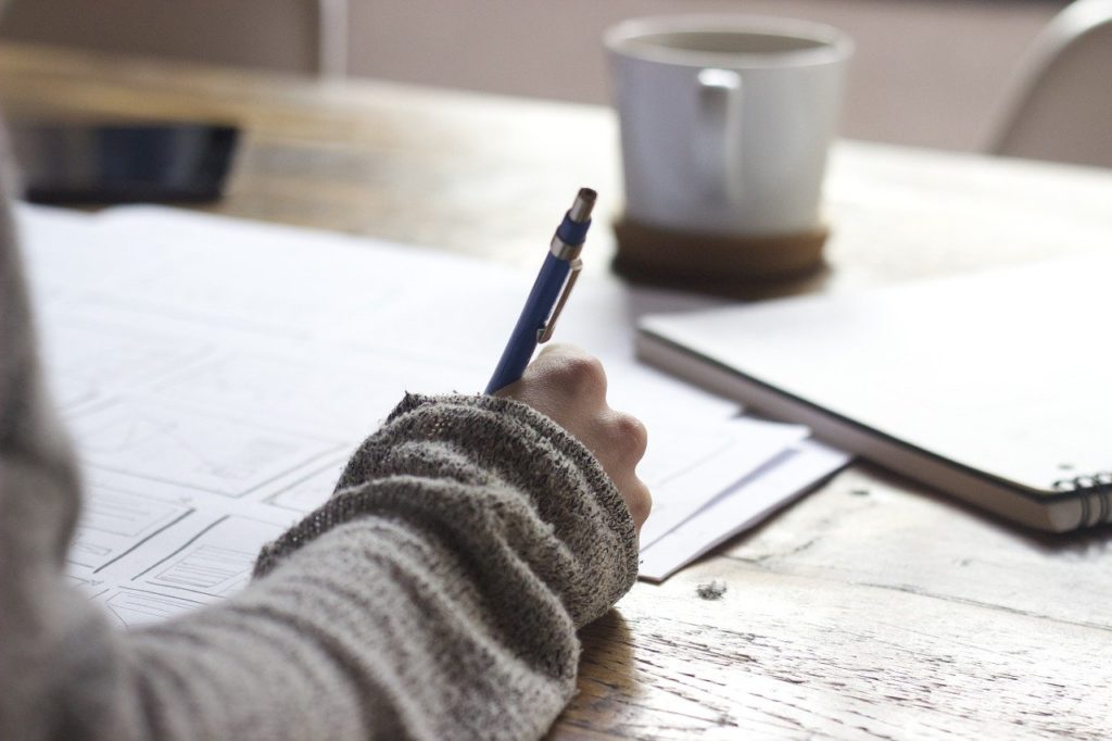 Arm in sweater holding a pen in front of a coffee cup