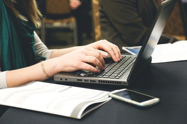 Hand extended over a PC laptop's keyboard with a workbook and phone sitting beside it.