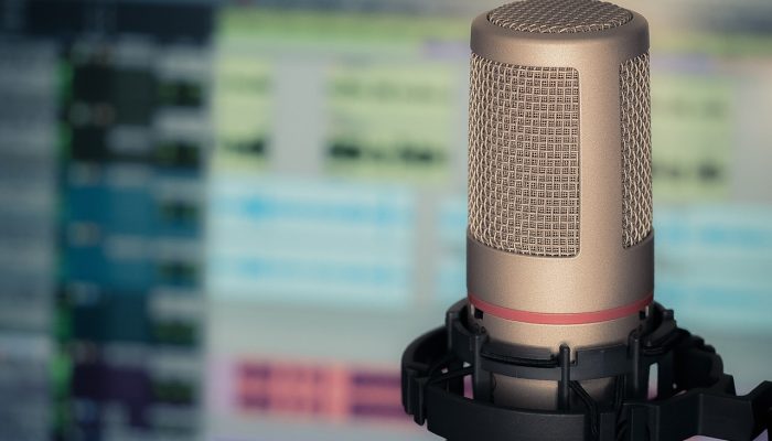 Picture Of A Microphone In The Foreground And A Blurry Computer Screen With Audio Editing Software In The Background